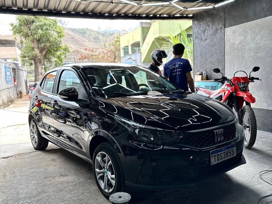Cliente conversando no box da Garage CleanCar ao lado de um Fiat Argo preto recém-polido