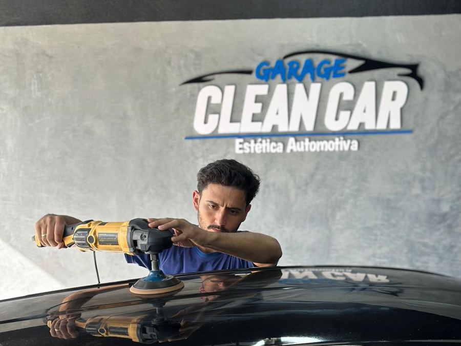 Profissional da Garage CleanCar polindo o teto de um carro preto com politriz, sob o letreiro da loja