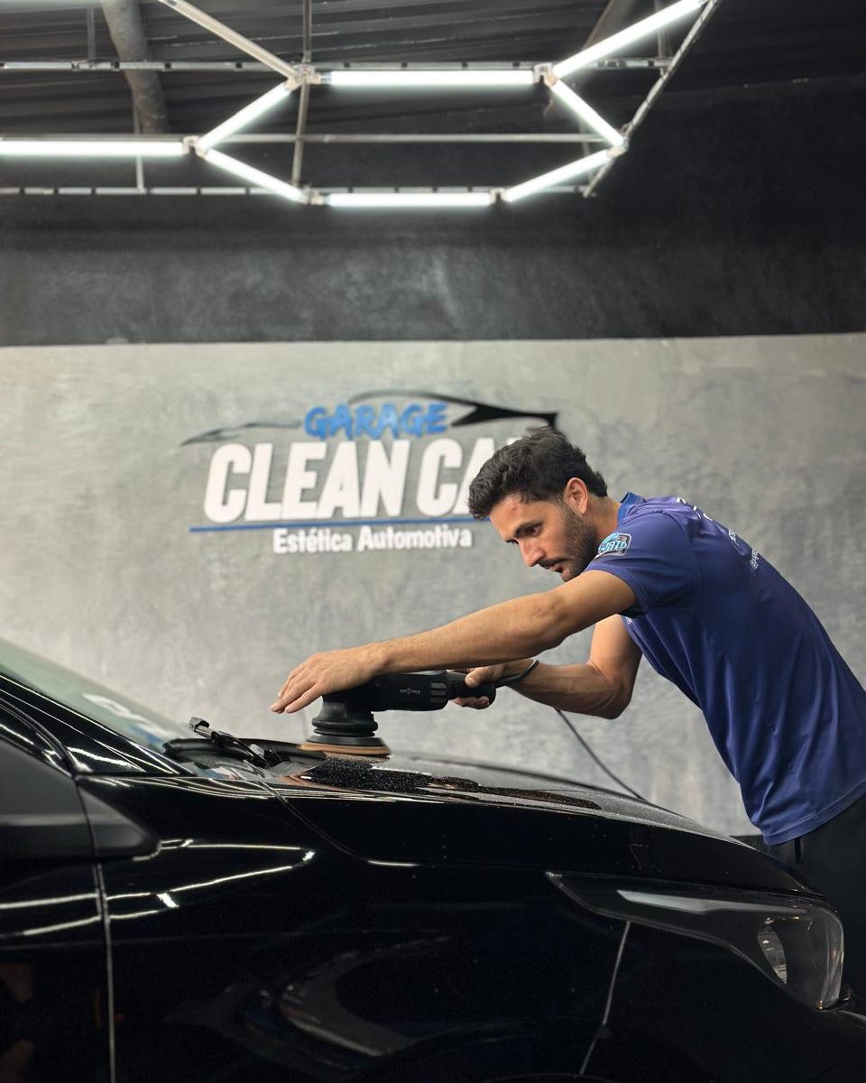 Profissional da Garage CleanCar polindo o capô de um carro preto sob o letreiro da loja