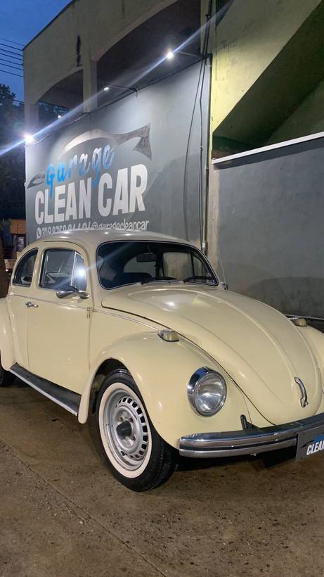 Fusca creme com pneus faixa branca em frente ao letreiro da Garage CleanCar à noite